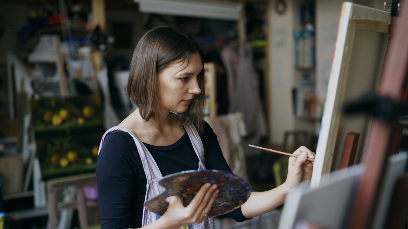 Artist painting on canvas in a studio setting.